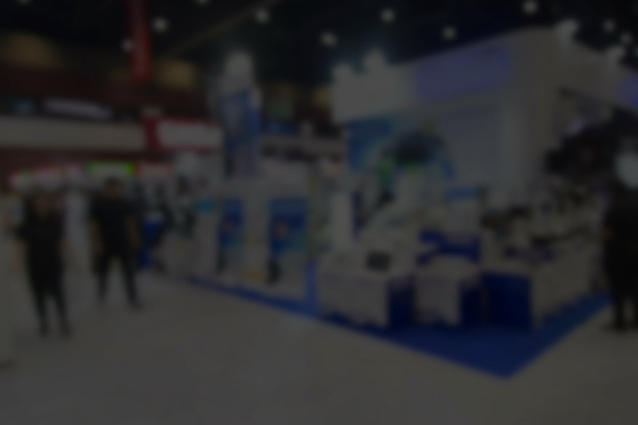 Blurred image of a trade show or exhibition with booths and people.